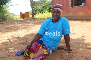 A woman in Mary's Meals t-shirt sits on the ground