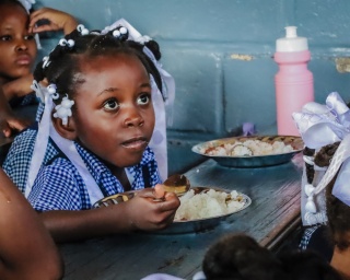 A girl in Haiti eats from a bowl in a classroom