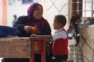A mother hands an orange to her son