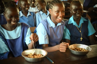Children smile while eating a bowl of food