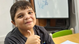 A young boy smiling and putting his thumb up