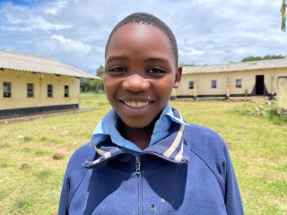  A young girl, Gugulethu, stands in front of her school smiling