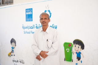 A man, Mr Yasser, stands in front of a Mary's Meals mural