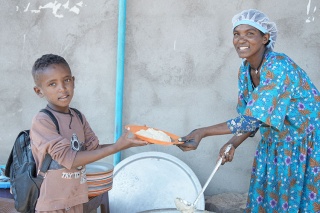 An image of a volunteer giving a school meal to a child