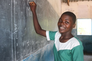 An image of a child in class writing on a chalkboard
