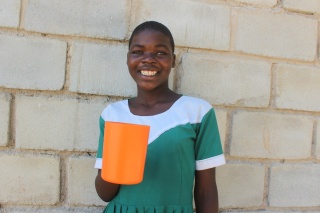 A happy girl stands next to a wall holding a mug