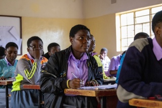 A girl sits in at a desk in a classroom with other children
