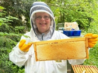 A woman in a beekeeping outfit holding honeycomb