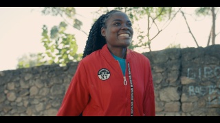 A young woman wearing a red jacket stands outside and smiles
