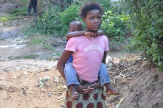 A young girl carries a younger boy on her back