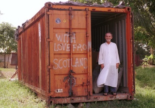 Father Garry stands in front of the Mary's Meals food container which says 'From Scotland with Love'
